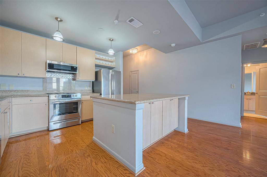 Modern kitchen with light wood cabinetry, granite countertops, and stainless steel appliances. Features an island with ample storage, hardwood floors, and recessed lighting for a bright, welcoming space.