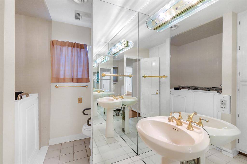 The hall bathroom was renovated at some time, but is a great candidate for further updating.  Currently, it features a stand-up sink with gold tone faucet hardware and mirrored surround.  There is also a commode, and then a walk-in bath suitable for elderly or handicapped.