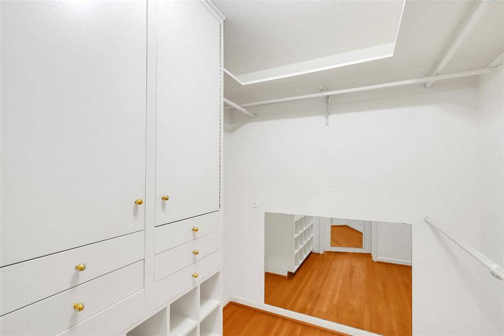 Inside the Primary closet showing built-in cabinetry, drawers, and shoe storage.  Beyond are multiple hanging racks.  For a home of this age, it really is a better than usual size Primary closet!