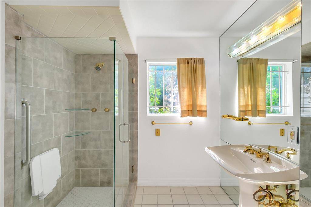 The primary bath features a single pedestal sink, large glassed-in shower with grab bar and glass shelving, and a commode (not seen).  The window views out to an unused portion of the rear yard.  Much as the bedroom, the side wall of the bathroom is mirrored floor to ceiling.