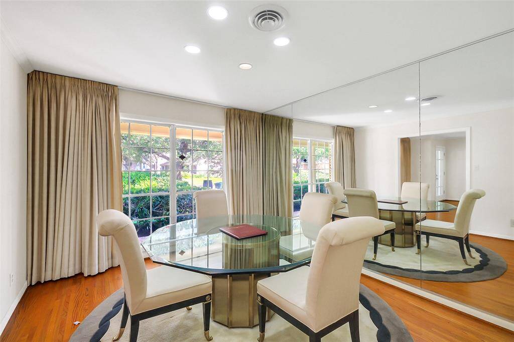 The formal dining area views also out to the front yard and neighborhood beyond.  Above, there is recessed lighting, and below are the warm tone real hardwood flooring.  A mirrored accent wall provides a sense of expansion.