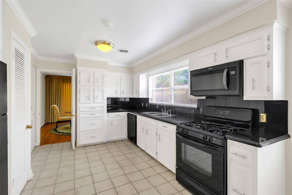 The light and bright black and white kitchen features crown molding, revised cabinetry, black granite counter tops, dual well stainless-steel sink, and black appliances including dishwasher, microwave, and gas range/oven.
