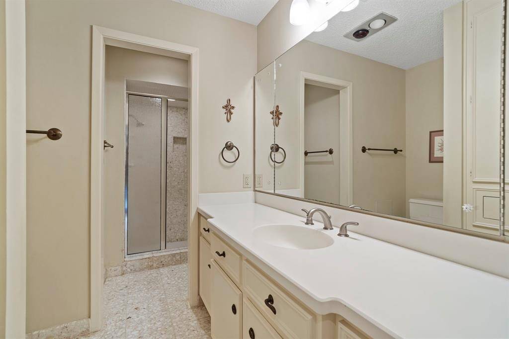 The secondary bedroom’s en suite bathroom features a walk-in shower with a sleek Terrazzo tile surround that matches the Terrazzo flooring, along with a spacious vanity that combines style and practicality.