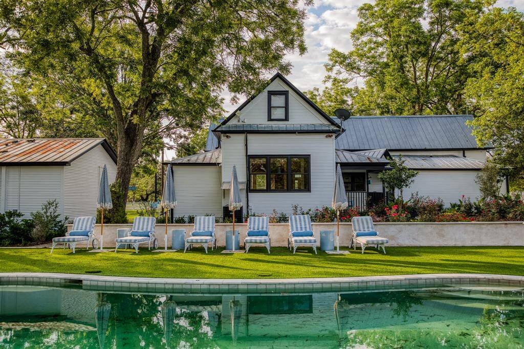 Framed by mature oaks & lush landscaping, the poolside view of The Cotton Pearl captures the effortless charm of this Round Top retreat. Blue-striped loungers & fringe umbrellas create a resort-like atmosphere for slow mornings or sunset gatherings.