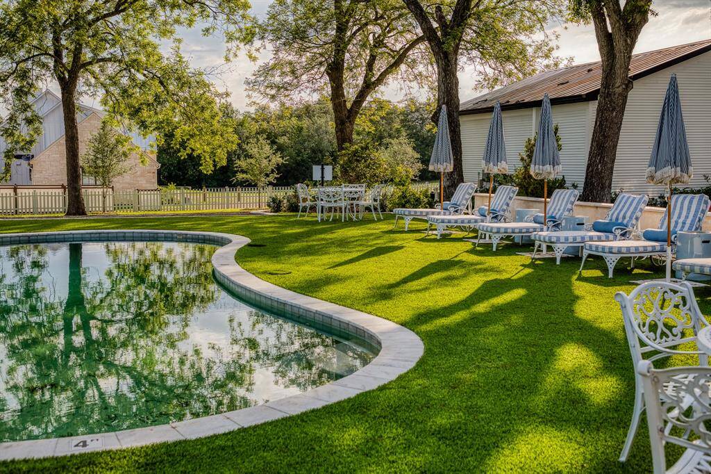 This side angle reveals the curved elegance of the pool framed by striped loungers and cast iron tables or gathering. Sitting in 2.23 acres, this high-end retreat provides a warm atmosphere.