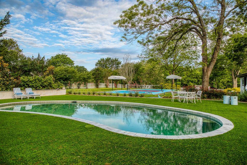 The oval-shaped pool and pickle ball court serve as the focal point of this outdoor retreat—a patio table, umbrellas, & loungers—dot the landscape. The backyard offers a perfect mix of relaxation & function, ideal for both everyday enjoyment & entertaining.