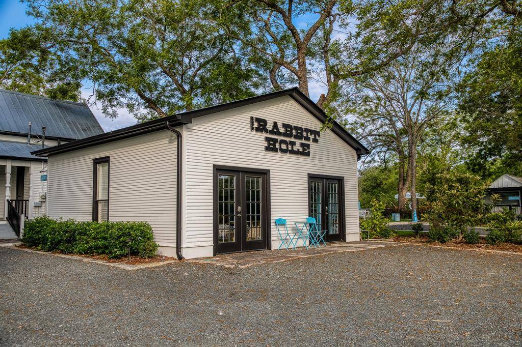 The Rabbit Hole’s crisp exterior and iconic black trim welcome guests with charm, while the generous gravel lot provides ample parking or room for creative outdoor setups—perfect for events that spill out under the trees.