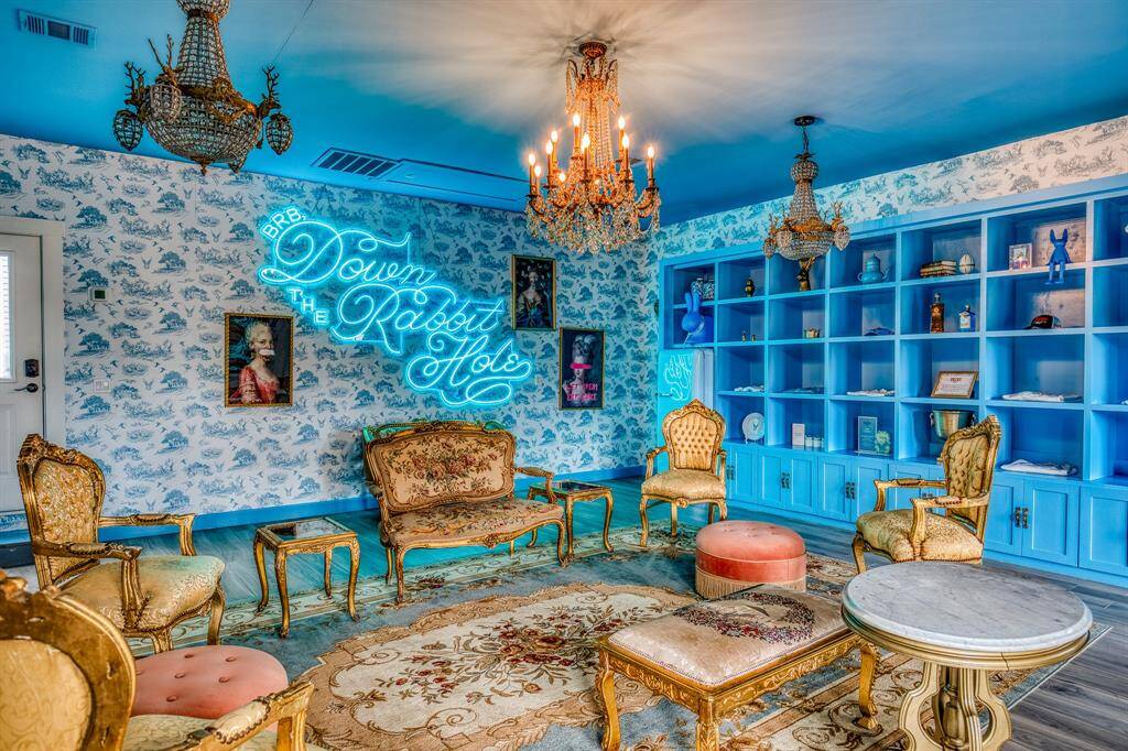 Gilded finishes and chandeliers add a dose of glamour to the eclectic charm of this vibrant lounge space, while the custom neon sign brings a playful flair to the room.