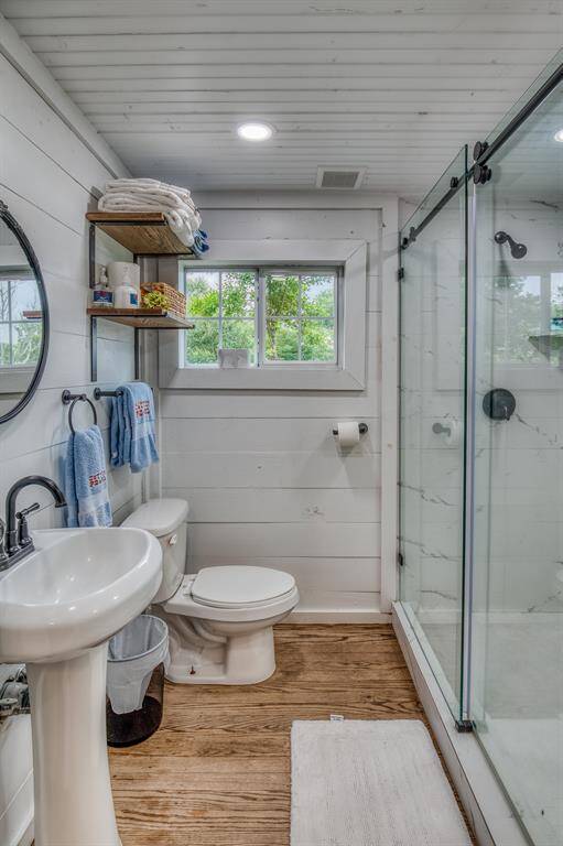 Clean lines and classic touches define this charming bathroom, featuring a glass-enclosed shower, pedestal sink, and warm wood floors.