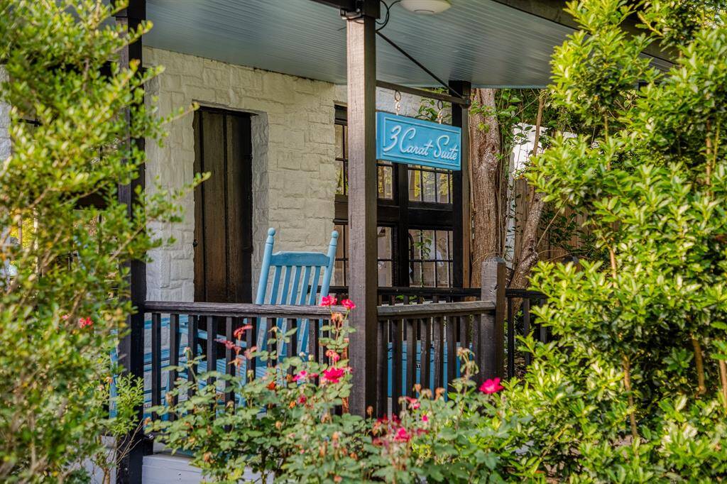 Nestled behind blooming roses and privacy hedges, the 3 Carat Suite welcomes guests with its shaded porch, bright blue rocking chair, and vintage signage.