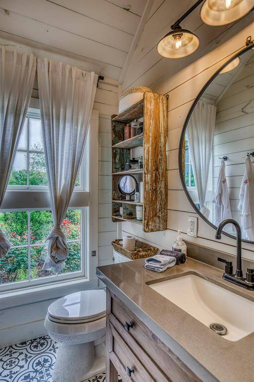 This light-filled bathroom is both functional and full of character, with rustic shelving, patterned tile floors, and a large window that brings the outdoors in.