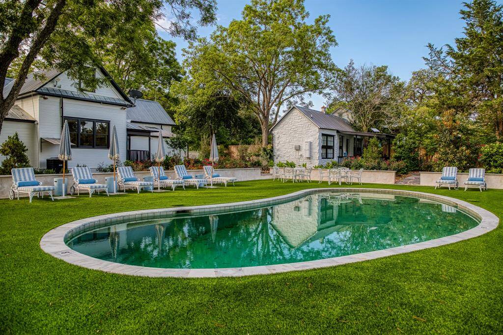 This wide-angle view captures the heart of the property—main home, stone guest house, & pool in perfect harmony. Surrounded by vibrant landscaping & dappled sunlight, it’s a peaceful portrait of laid-back Texas luxury.