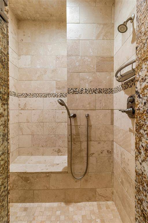 Primary Bedroom-Private En Suite Bathroom Shower. Frameless glass door. Travertine walls and mosaic details. Thoughtfully designed for luxury and comfort with a built-in bench and two showerheads.