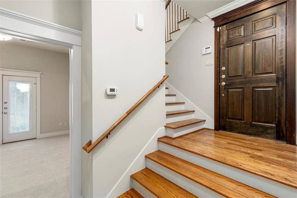 Interior Entryway of home. Dark wood front door contrasts nicely with white walls. Hardwood staircase with simple wooden handrails lead to the upper floors. 1st floor Bedroom is seen to the left with a glass paneled exterior door leading to side yard.