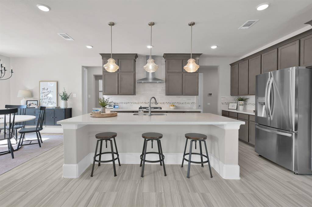 Gourmet kitchen features built-in appliances including 4-burner gas cooktop, expansive island perfect for entertaining, upgraded pendant lights, shaker-style cabinetry, and a bright breakfast/dining nook.