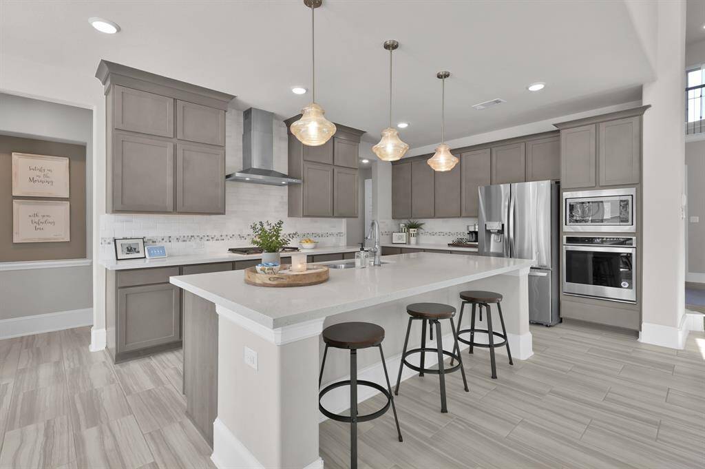Gourmet kitchen features built-in appliances including 4-burner gas cooktop, expansive island perfect for entertaining, upgraded pendant lights, shaker-style cabinetry, and a bright breakfast/dining nook.