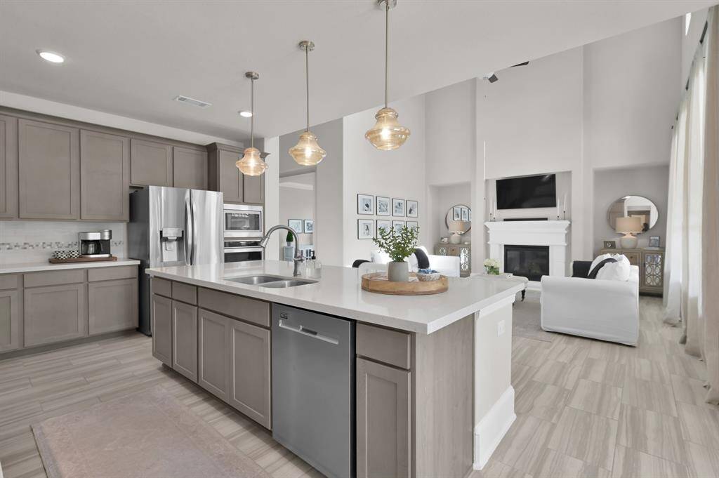 Gourmet kitchen features built-in appliances including 4-burner gas cooktop, expansive island perfect for entertaining, upgraded pendant lights, shaker-style cabinetry, and a bright breakfast/dining nook.