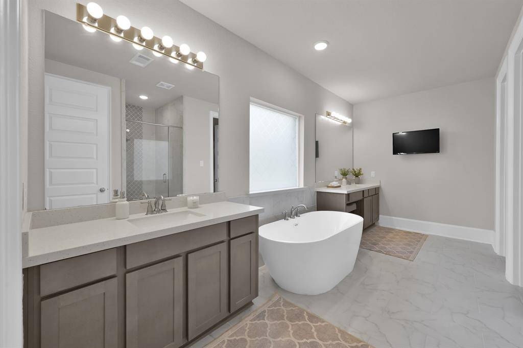 Spa-like en-suite bathroom featuring dual vanities, a standalone soaking tub, oversized, Texas-sized walk-in shower with upgraded tile, and two large walk-in closets.
