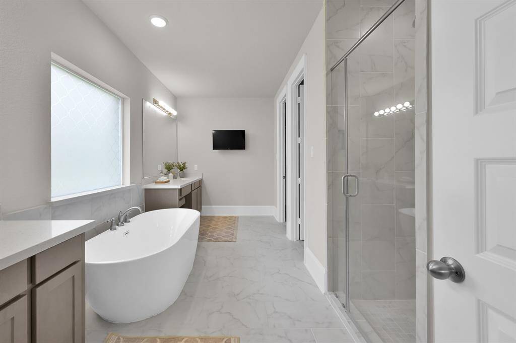 Spa-like en-suite bathroom featuring dual vanities, a standalone soaking tub, oversized, Texas-sized walk-in shower with upgraded tile, and two large walk-in closets.