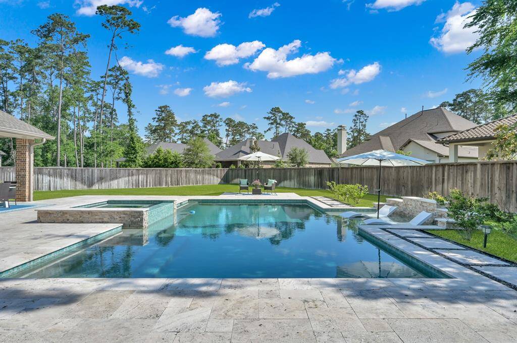 This luxury pool & spa features a raised spa with spillover edge, tanning ledge with umbrella sleeve, rock wall feature, travertine decking, and durable, low-maintenance PebbleTec surface.