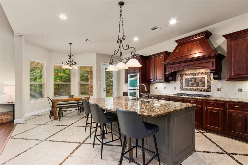 The chef's kitchen with center island boasts gorgeous tiled flooring, granite countertops with coordinating backsplash, and handsome, raised panel cabinetry.