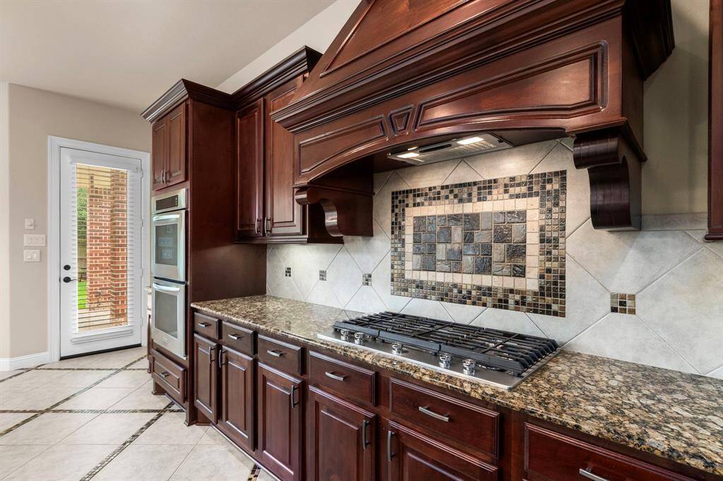 A custom-designed tile backsplash behind the Kitchen Aid 5 gas burner and underneath the custom hood vent adds to the kitchen's wonderful aesthetic appeal.
