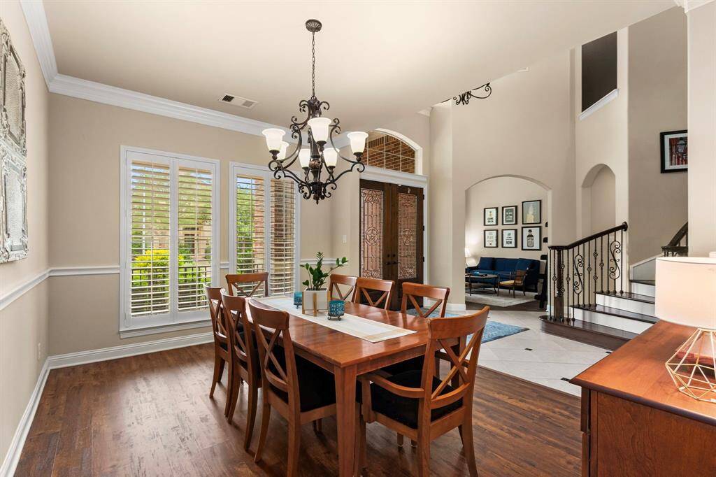 Another look at the formal dining room with large, plantation shuttered windows that overlook the front lawn and a beautiful, designer chandelier. Across the front entry and through the large arched opening is the spacious sitting room.