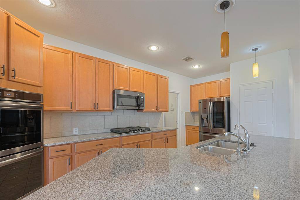 Modern kitchen with ample wooden cabinetry, granite countertops, and stainless steel appliances. Features a central island with a sink and pendant lighting, creating a bright and functional space.
