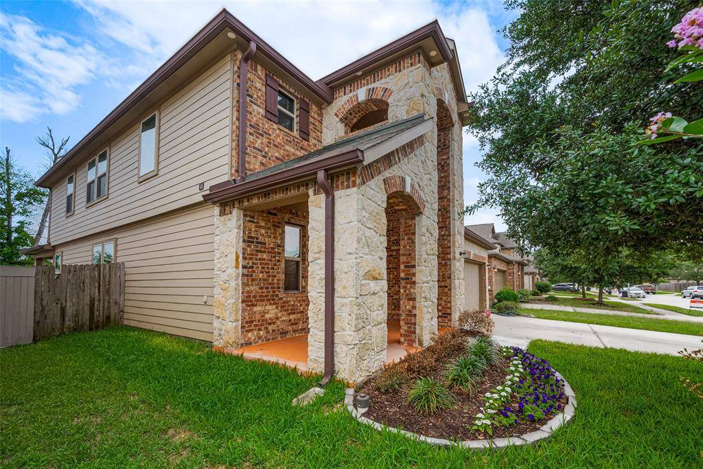 This photo showcases a charming two-story house with a brick and stone facade, complemented by a small, well-maintained front garden. The home features a covered porch and is situated in a suburban neighborhood with a tree-lined street.