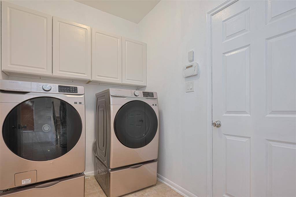 This laundry room features modern, front-loading washer and dryer units with storage cabinets above. The space is well-lit with a clean, white finish, offering a functional and organized area for laundry tasks.
