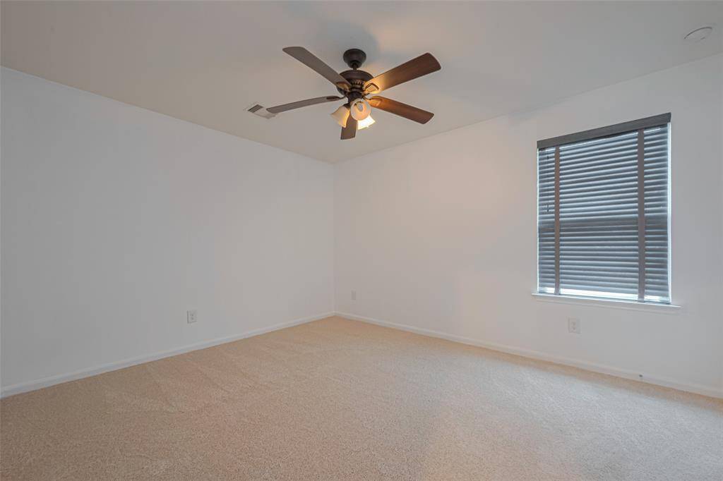 This room features neutral carpeting, white walls, a ceiling fan with lights, and a window with blinds, offering a bright and versatile space.