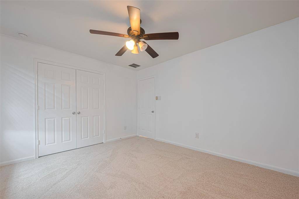 This is a bright, freshly-painted bedroom with neutral carpeting, a ceiling fan, and a double-door closet, offering ample storage space.