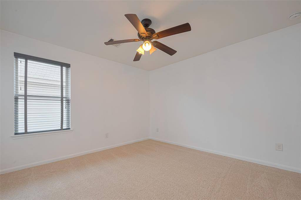 This room features neutral walls, soft carpeting, a ceiling fan with lights, and a window with blinds, offering a comfortable and inviting space.