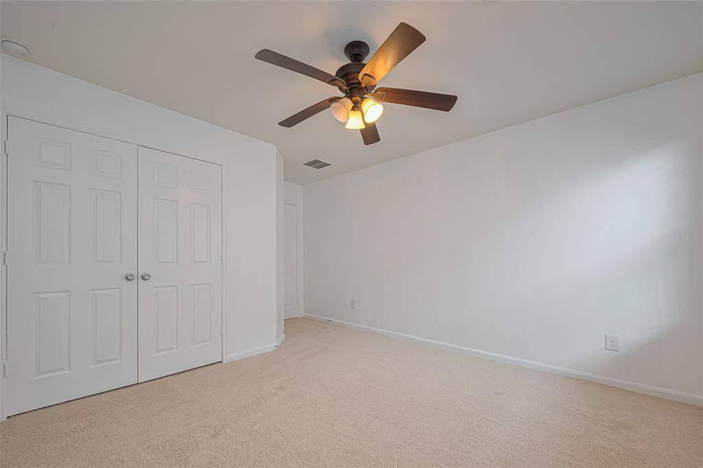 This room features neutral carpeting, a double-door closet, and a ceiling fan with lights, providing a clean and bright space ideal for a bedroom or office.