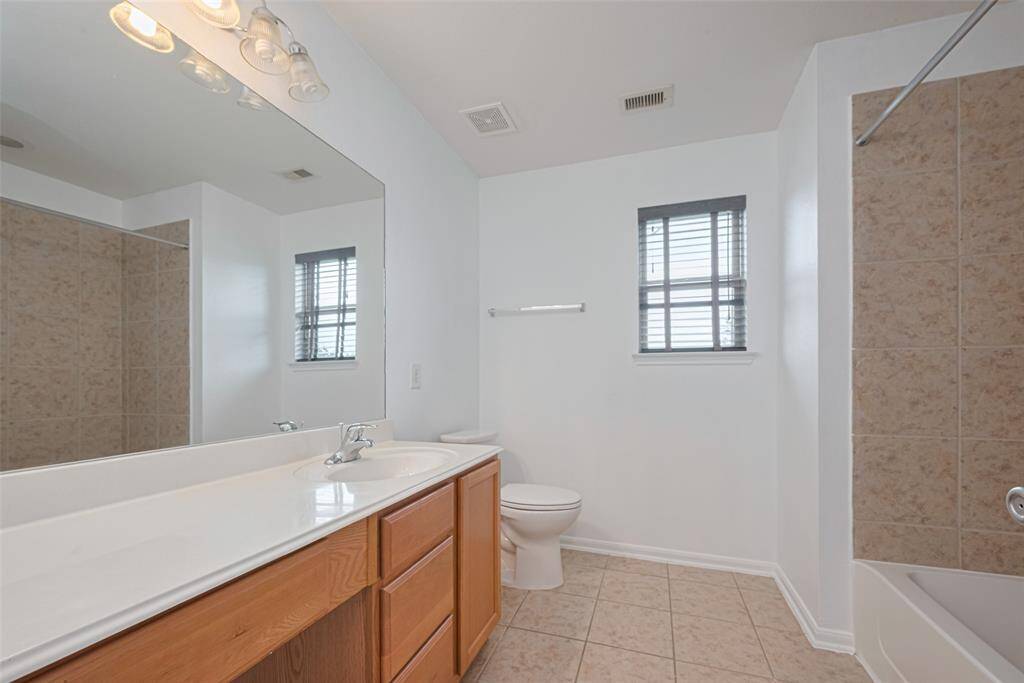 This bathroom features a clean and spacious design with a large mirror, wooden vanity, and ample counter space. It includes a bathtub with tiled surround and a window for natural light.
