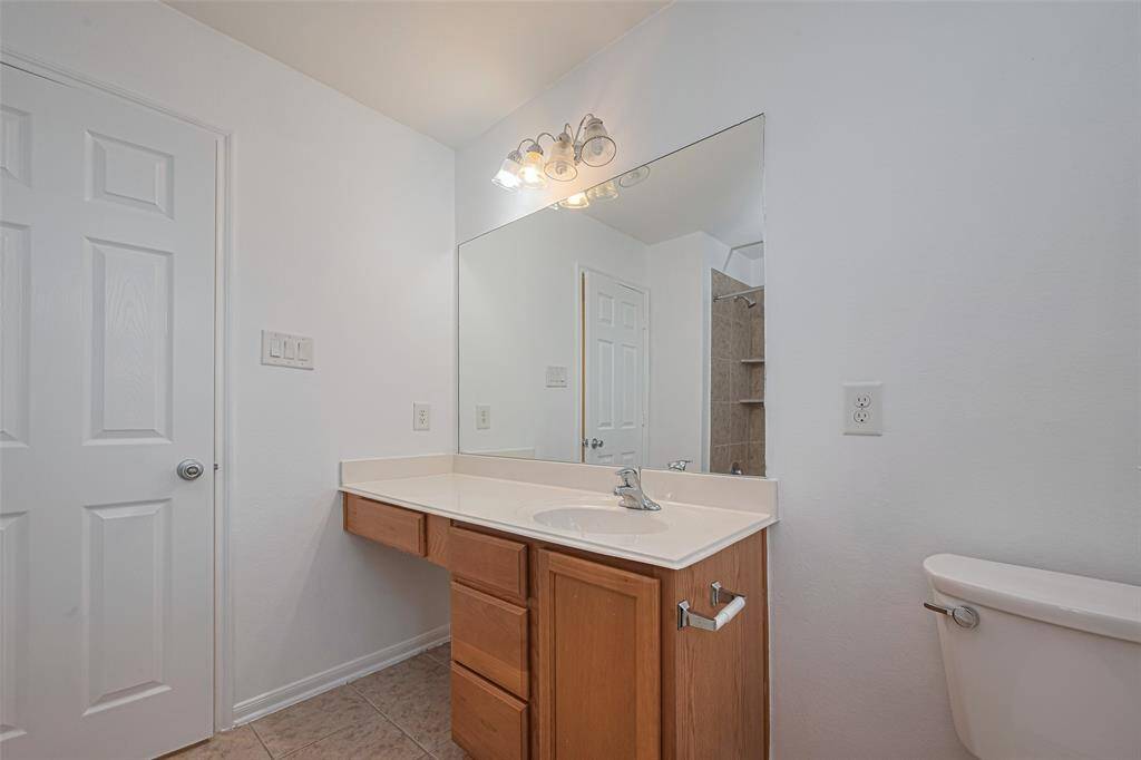 This bathroom features a clean and simple design with a large mirror, ample counter space, wooden cabinets, and a toilet. The neutral color palette and tiled flooring add a modern touch.