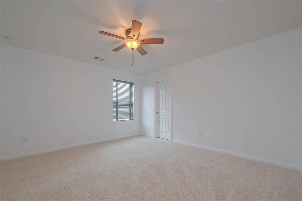 Bright, spacious bedroom with neutral carpet, a ceiling fan, and a window for natural light. Features a clean, minimalist aesthetic with a small closet.