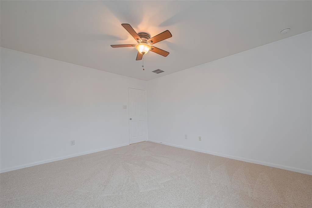 This room is spacious with neutral carpet and walls, featuring a ceiling fan with light. It has a simple, clean design with a door and electrical outlets visible.
