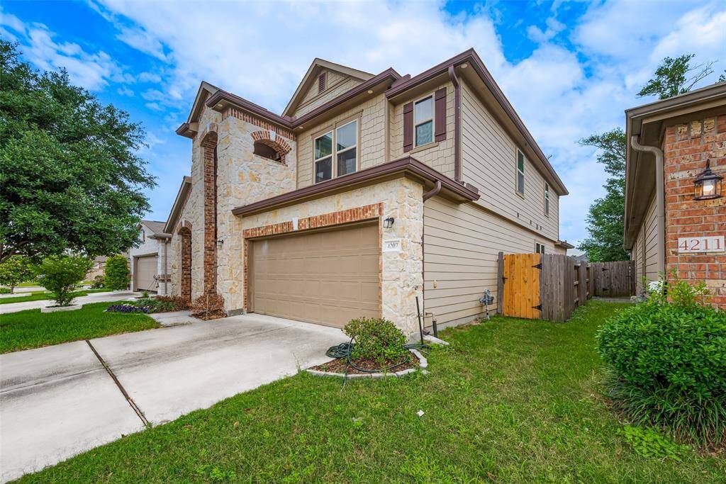 This is a modern two-story home with a stone and brick façade, featuring a two-car garage and a neatly maintained front lawn. The property is situated in a suburban neighborhood with a fenced backyard and a paved driveway.