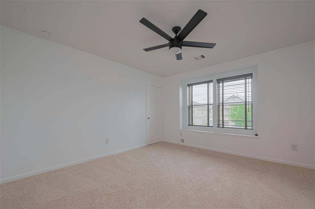 This room features neutral carpet and white walls, with a modern black ceiling fan. A large window provides natural light, and a closet is tucked into the corner, creating a clean and bright space.