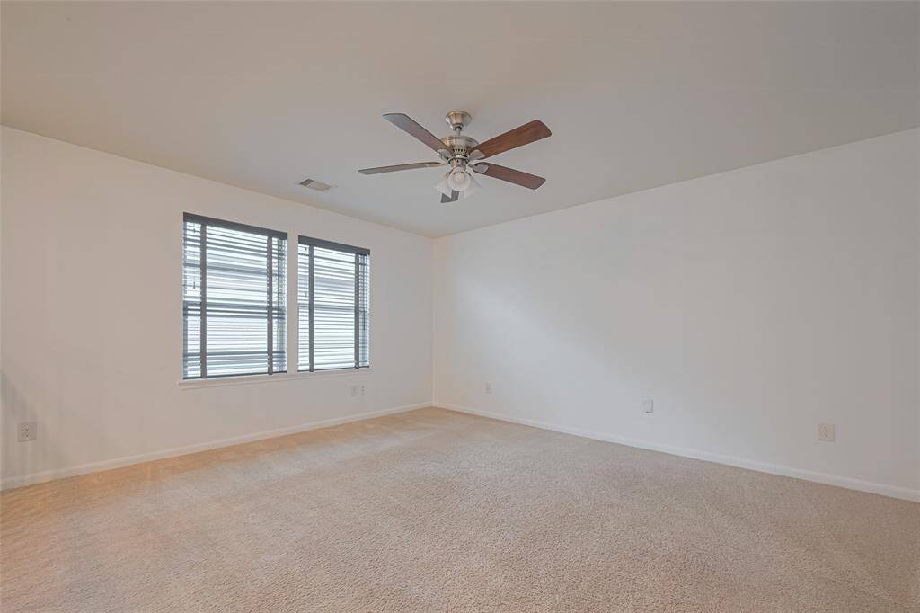 This room is spacious and bright, featuring neutral-colored carpeting, a ceiling fan, and large windows that allow plenty of natural light. Ideal for a bedroom or living area.