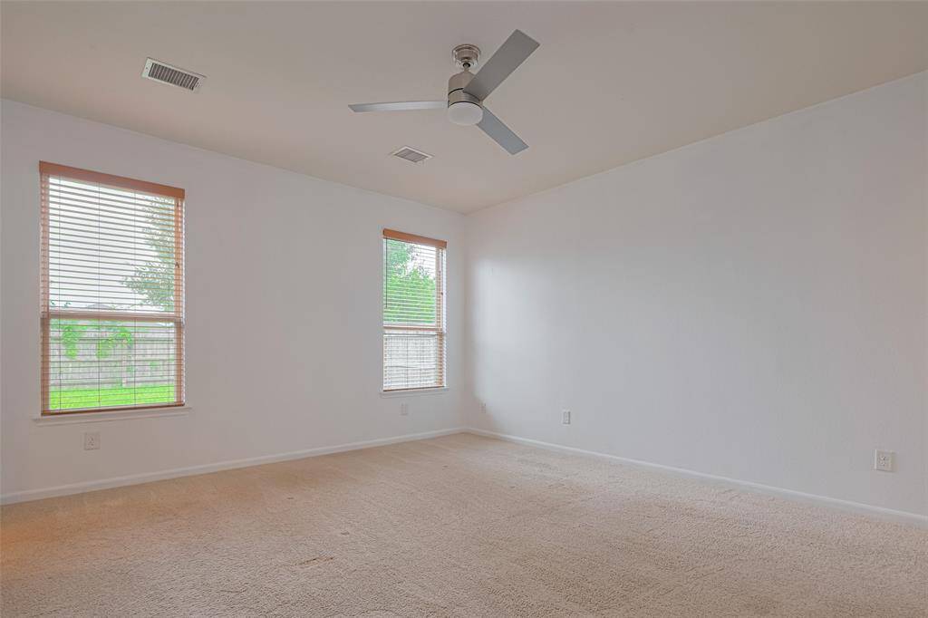 Bright, spacious room with neutral carpet, two large windows offering plenty of natural light, and a modern ceiling fan. Ideal for a bedroom or office.
