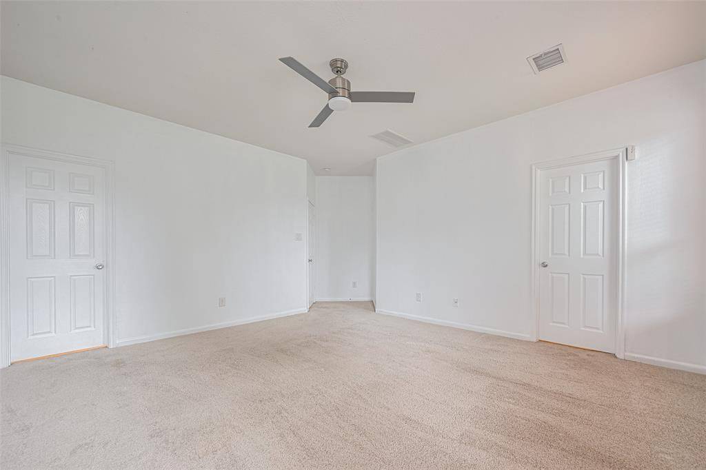 A spacious, carpeted room with neutral walls and ceiling, featuring a modern ceiling fan and two doors. Ideal for a bedroom or office space.