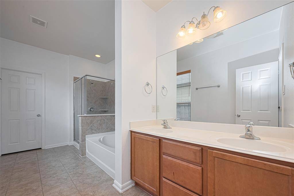 This bathroom features a spacious layout with neutral tile flooring, a large double vanity with wooden cabinets, a glass-enclosed shower, and a separate bathtub. The space is well-lit with overhead fixtures and has a clean, modern look.