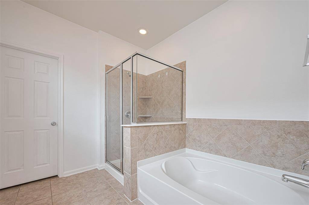 This bathroom features a clean, modern design with a spacious glass-enclosed shower and a separate soaking tub. The neutral tile and white walls create a bright and inviting atmosphere.