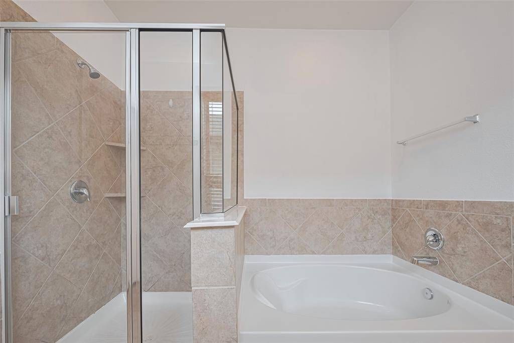 This bathroom features a modern design with a glass-enclosed shower and a separate bathtub, both surrounded by neutral-toned tile for a clean and elegant look.