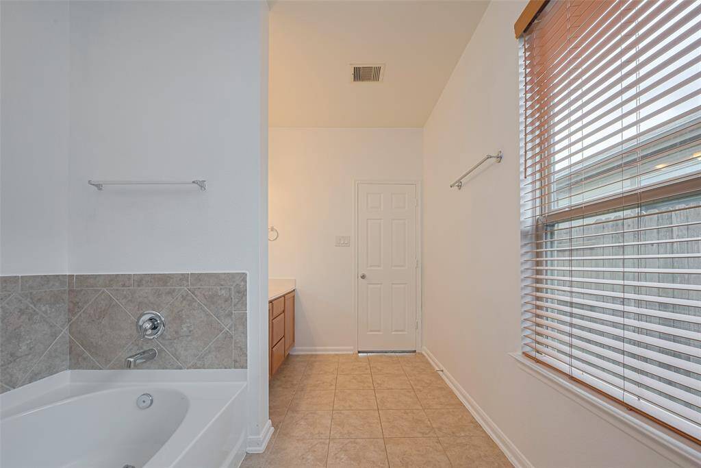 This bathroom features a large bathtub with tiled walls, a window with blinds for natural light, and a spacious layout with neutral tones.