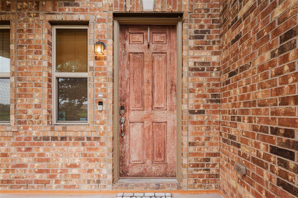 Charming brick exterior with a rustic wooden front door, complemented by a side window and a welcoming porch light.