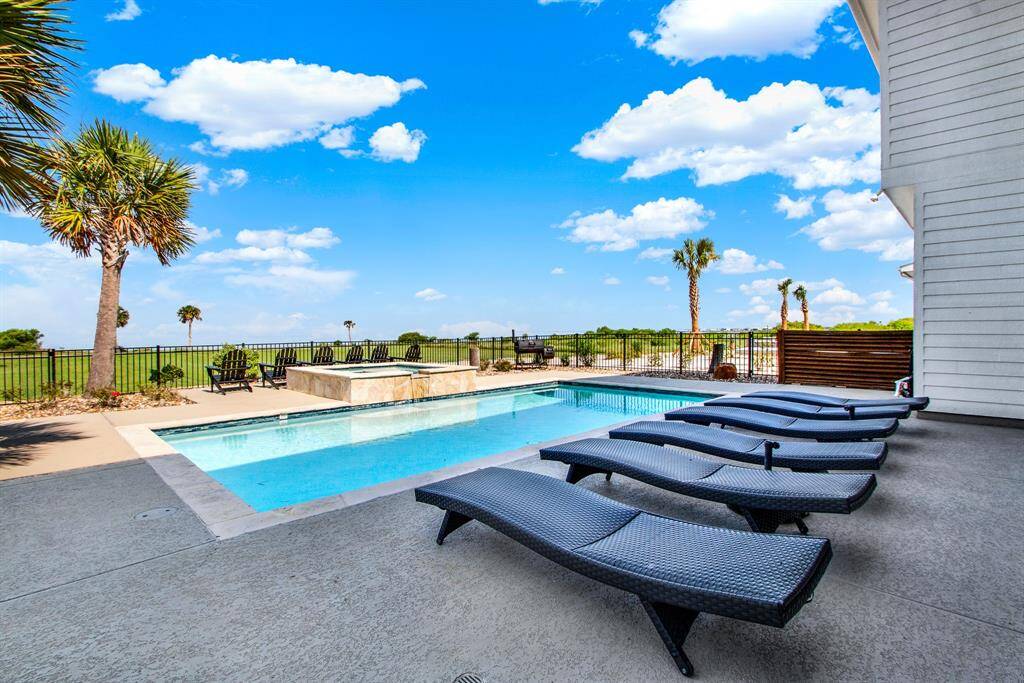 This is a spacious outdoor area welcomes you and your guests into the swimming pool with ample poolside lounging options, complemented by picturesque palm trees and a clear blue sky, offering a perfect setting for relaxation and entertainment.