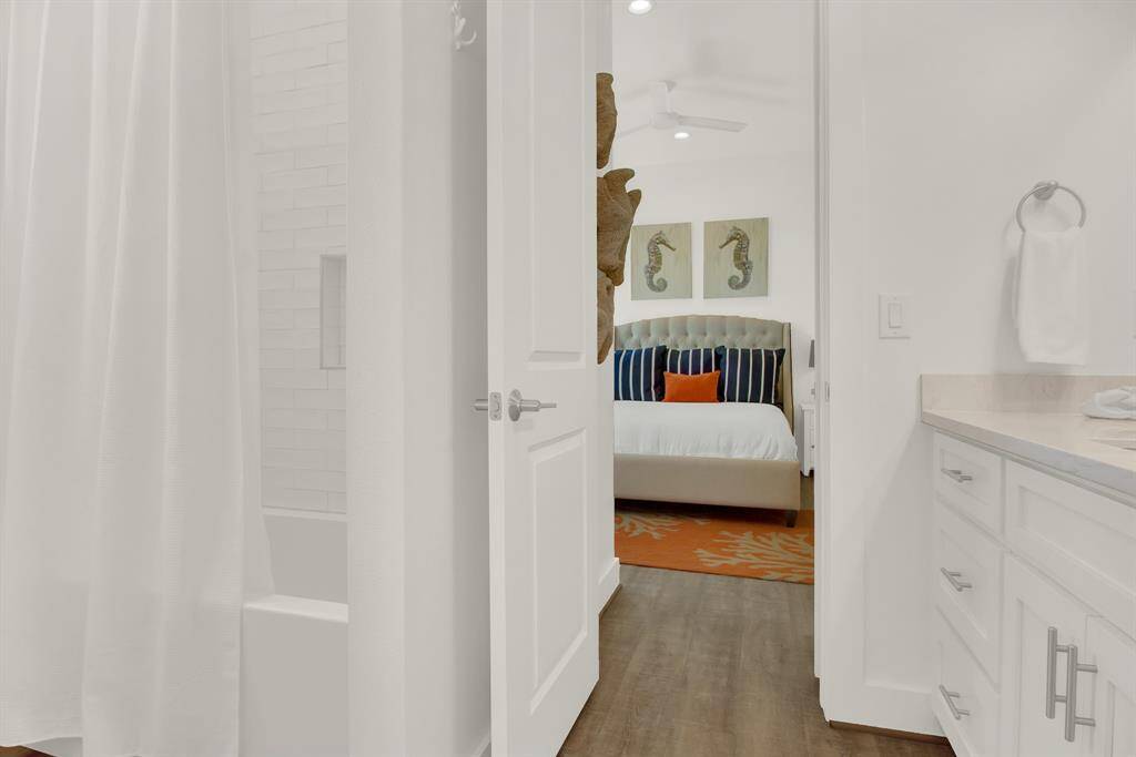 This is a modern en-suite with a seamless transition from a bright bathroom featuring white cabinetry and subway tiles to a cozy bedroom with ample space for any sized bed and luxury vinyl plank floors throughout the home.